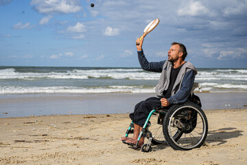Disabled man sitting on a wheelchair playing paddle ball on the beach