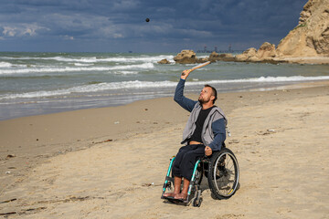 Disabled man sitting on a wheelchair playing paddle ball on the beach