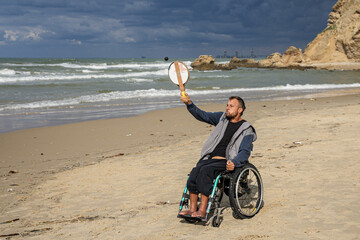 Disabled man sitting on a wheelchair playing paddle ball on the beach