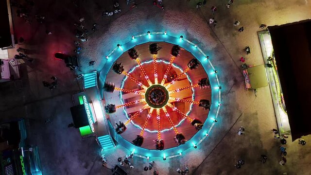 State fair at night time aerial view. Drone flight over blinking neon lights with carousel ride at carnival in Portugal. 