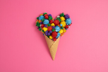 Colorful pom-poms in ice cream cone on pink background. Minimal concept. Flat lay.