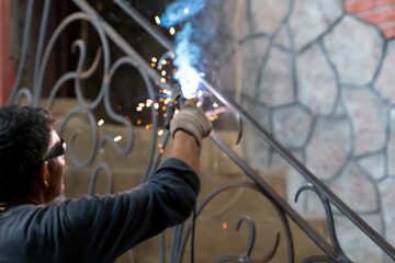 Man in safety glasses is welding metal of staircase. Welding work on metal in private house. blurred background. Close-up.