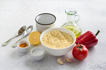 Ingredients for vegan chickpea omelette: chickpea flour, red bell pepper, tomato, garlic, lemon, water, olive oil and spices on light gray table. Cooking