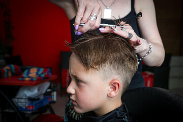 Close-up of a cute little boy while hairdresser cutting his hair using scissors and comb