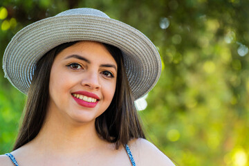 Young woman at park using a hat and dress during summer spring season at a sunny day. Brunette with long black hair.