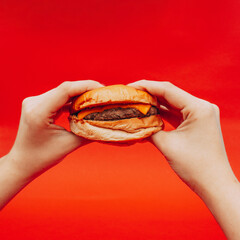 Fototapeta Hamburguesa deliciosa comida rápida sostenida con la mano de mujer con fondo rojo obraz
