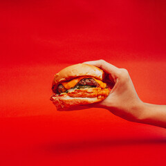 Hamburguesa deliciosa comida rápida sostenida con la mano con fondo rojo