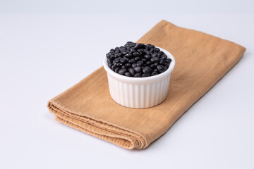 Fototapeta na wymiar black bean in white bowl on cloth and white background studio shot