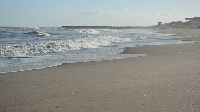 Playa, olas y a lo lejos, pescadores en el espig&oacute;n lanzando