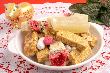 Candy comfit, Chinese sweetmeat or snack made of rice crispy bars, candied winter melon on white dish with white lace placemat and Golden Cow doll decoration for Year of Cow