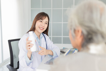 asian female doctor explaining about how to use medicine with old patient in hospital, elderly disease treatment, she holding drug bottle with hand