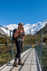 New Zealand female hiker on a bridge on the alpine track to Mount Cook with the snowy mountain in the back