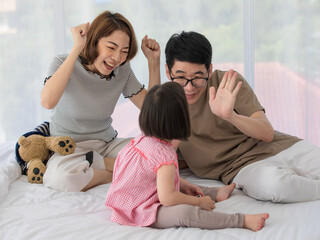 Asian lovely family father and mother in casual wears sitting on bed playing children toys and teddy bear doll with little cute happy active down syndrome autistic autism daughter in bedroom at home