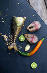 smoked mackerel fish with spices, pepper and lime on dark background. Smoked fish, mediterranean food, herring fish, seafood, top view