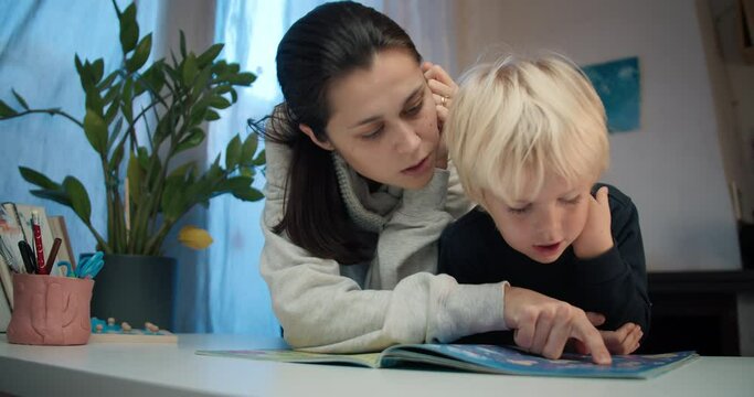 Family young mother with son together reading the book. Attractive woman helping to her child pass the labyrinth. Concept go preschool children education and growth
