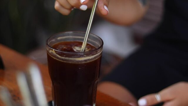 woman's Hands stirring  refreshing iced coffee in a glass. wooden table. close up shot