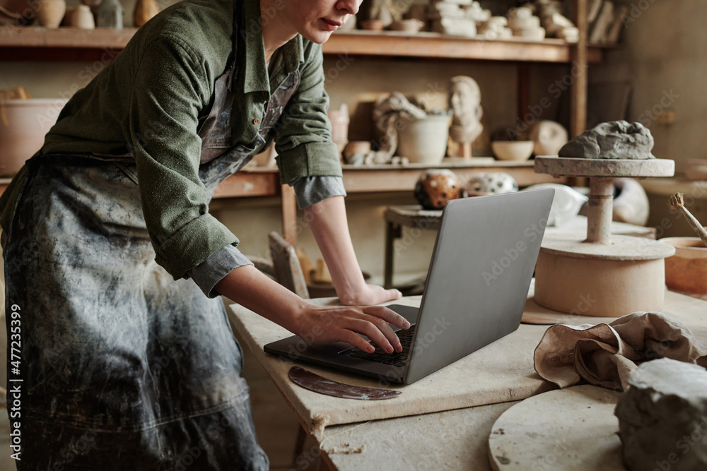 Wall mural Close-up of craftsperson typing on laptop and creating new models online in the ceramic studio