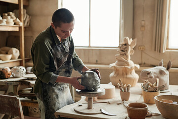 Young sculptor making form from the clay to make beautiful sculptures in workshop - obrazy, fototapety, plakaty