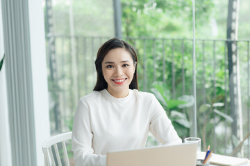 Young cheery happy positive cute beautiful business woman sit indoors in office using laptop computer.