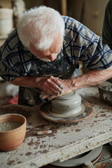Close-up of senior potter modeling the vase from clay on pottery wheel in workshop