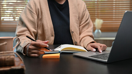 Young woman working with laptop and making notes on sticky notes.