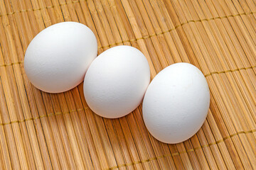 Three raw chicken eggs on a bamboo napkin close-up
