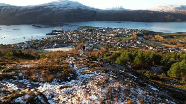 Adult Perched On Snow Covered Ground Overlooking Town Of Ullapool. Aerial Parallax