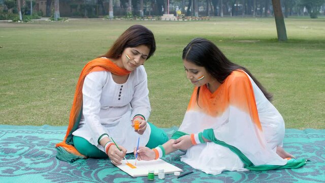 A beautiful mother and her young daughter making a sketch of the Indian National Flag. Pretty females dressed in white Kurtis and Tricolor Dupattas sitting outdoors - Republic Day  patriotism  Nati...