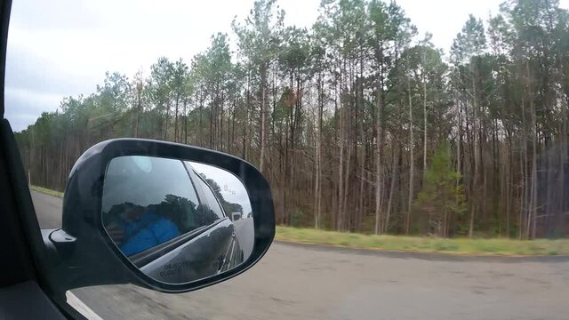 Driving along a highway and through a forest - hyper lapse of the passenger point of view out the window with a view the rear view mirror