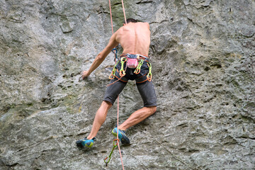 Young man climbing steep wall of rocky mountain. Male climber overcomes challenging route. Engaging in extreme sport concept