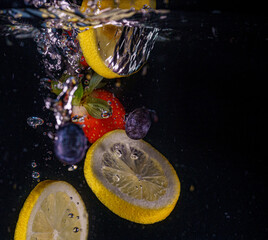 Red strawberries, yellow lemons and blueberries fall into the water. Water splash, drops. Slow...
