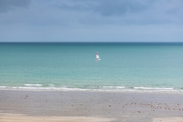 Beautiful beach at Agon-Coutainville in Normandy, with a sailing boat on the sea
