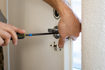 Closeup of a locksmith installing or repairing a new deadbolt lock on a house exterior door. Man...