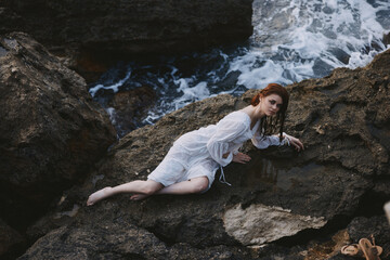 beautiful young woman in long white dress wet hair lying on a rocky cliff unaltered
