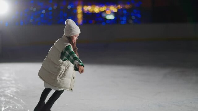 It's winter time, a little girl skates, performs the elements of figure skating at the rink.