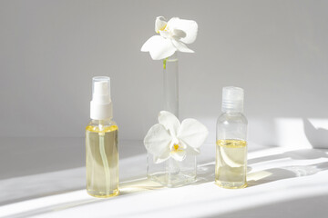 Two transparent glass bottles with spray caps and orchid flowers on white background in morning...