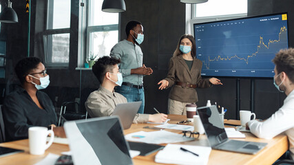 Colleagues having meeting in boardroom, woman in mask making presentation