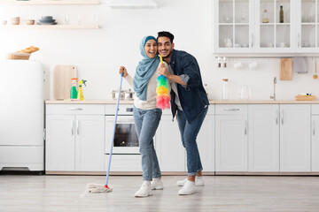 Loving muslim couple cleaning floor and having fun in kitchen