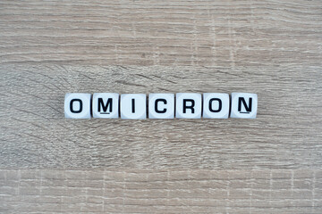 A white cube written Omicron over wooden table. New Variant. Coronavirus Mutation