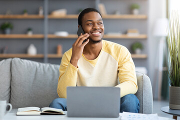 Joyful black guy freelancer having phone conversation