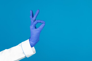 Doctors hand in a glove holds with OK gesture on a blue background with copy space