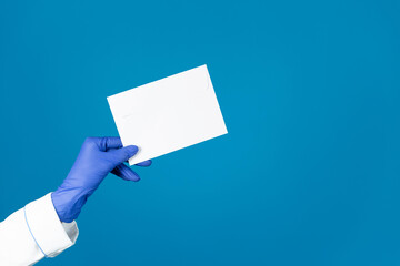 Doctors hand in a glove holds an envelope on a blue background with copy space