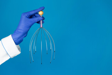 Doctors hand in a glove holds a antistress massager from headache on a blue background with copy space