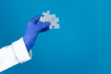 Doctors hand in a glove holds a puzzles on a blue background with copy space