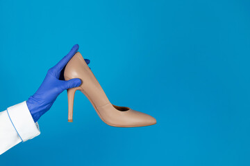 Doctors hand in a glove holds a high heels shoes on a blue background with copy space