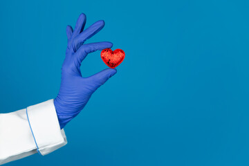 Doctors hand in a glove holds a heart on a blue background with copy space. world heart day, world blood donor