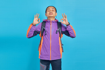 Portrait of handsome man smiling casually with closed eyes doing meditation gesture with finger over blue background