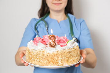 The doctor or nurse holds a birthday cake with the number three for the anniversary of the opening of the clinic