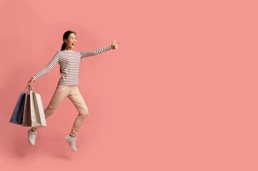 Shocking Sales. Excited Asian Woman Jumping With Shopping Bags And Pointing Aside