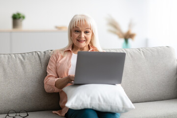 Happy mature woman sitting on couch and using computer
